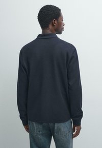 Mørkeblå langærmet polo med krave, afslappet pasform og ribbede ærmegab. Stoffet ser blødt ud med diskrete syningsdetaljer langs sømmene.