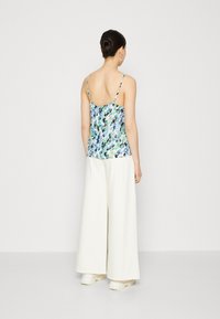 Débardeur à imprimé floral bleu, vert et noir avec des bretelles fines, associé à un pantalon large blanc et des chaussures blanches décontractées.