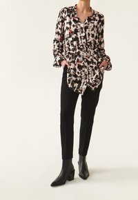 Camicia button-up con una stampa animalier nera, bianca e rossa, abbinata a pantaloni neri su misura e stivaletti neri con tacco.