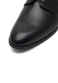 Juodas odinis batas su blizgiu paviršiumi, smailiu nosimi ir minimaliais siuvinėjimais, pasižymintis glotniu tekstūru ir plona padu.