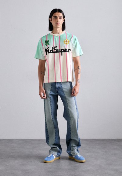T-shirt with mint green sleeves, cream body, pink stripes, and black "KidSuper" logo; worn with light blue denim jeans and blue sneakers.