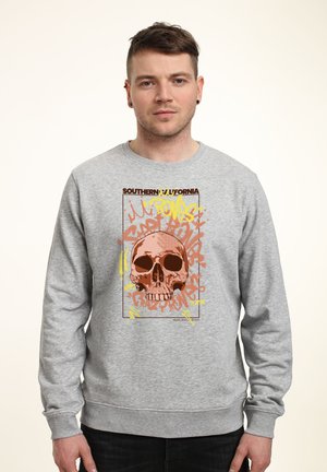 Grå sweatshirts med et frontmotiv af et kranium omkranset af farverig graffiti-stil tekst i gul, orange og rød. Blød tekstur.