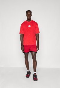 Rød bomulds T-shirt med et lille logo patch, parret med røde mesh shorts med sort kant. Sorte og røde atletiksko fuldender looket.