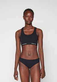 Soutien-gorge de sport noir avec des bretelles épaisses et une bande logoée ; bas de bikini noir assorti ; tissu lisse avec un ajustement serré.