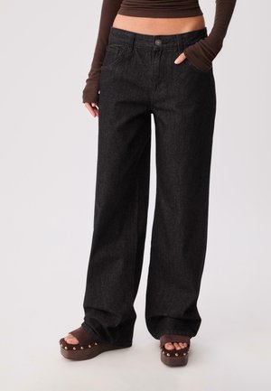 Black denim wide-leg pants with a high waist, featuring front pockets and a button closure, paired with brown platform sandals.