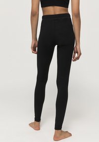 Zwarte high-waisted leggings van rekbaar materiaal, met een gladde textuur en een aansluitend ontwerp, afgebeeld van achteren met blote voeten.