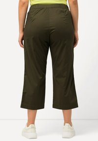 Olivgrön kort byxor med elastisk midja, slät textur, sida sprund och bärs med vita sneakers.