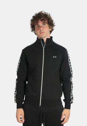 Felpa nera con zipper e colletto alto, con accenti bianchi a fantasia lungo le maniche, texture morbida e polsini aderenti. Logo minimalista sul petto.