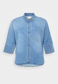 Camisa de ganga azul claro com gola dobrável, fecho de botões e bolso no peito. Apresenta mangas curtas e detalhes em ponta de prata na gola.
