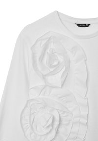 Camicia bianca a maniche lunghe con grandi applicazioni di rose in tessuto strati sul davanti. Materiale in cotone morbido con scollo a girocollo.