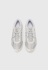 Scarpe sportive grigie con tomaia in mesh, lacci piatti e suola bianca. Presentano una punta arrotondata e linee di accento minime sui lati.