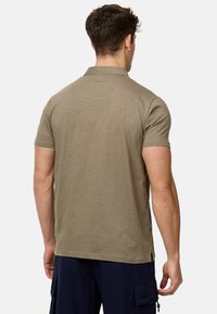Polo shirt à manches courtes vert olive avec un col classique et un tissu doux et texturé. Présente des fentes latérales et une coupe décontractée.