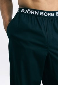 Fekete rövidnadrág széles, rugalmas derékrésszel, rajta fehér "BJÖRN BORG" felirattal. Az anyag simának és könnyűnek tűnik.