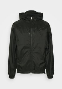 Svart lättviktig jacka med huva, framzipper och elastiska mudd. Slät, glänsande textur med dragsnoddar vid huvan och nederkanten.