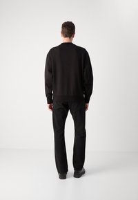 Felpa nera con collo rotondo e polsini a costine, abbinata a jeans neri a gamba dritta. Texture liscia, design minimale e senza motivi visibili.