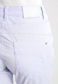 Ljusblå byxor sett bakifrån, med en sydd fickdesign och en etikett märkt "OPUS" ovanför midjan.