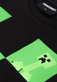 Black cotton T-shirt featuring a large green Minecraft-inspired creeper graphic with pixelated details, set against a contrasting black background.