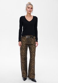 Czarny sweter w serek zestawiony z spodniami w leopardzi wzór o wysokim stanie i rozszerzanych nogawkach. Spodnie mają brązowe i czarne plamki na beżowym tle. W zestawie jest czarny pasek.