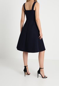 Granatowa sukienka w kształcie litery A z teksturowanej tkaniny, szerokimi ramiączkami i rozkloszowaną spódnicą. W połączeniu z czarnymi sandałami na wysokim obcasie.