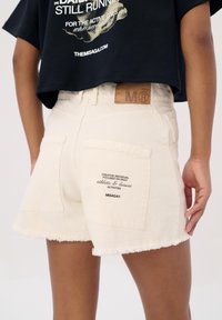 Witte denim shorts met een ruwe zoom, voorzien van twee achterzakken met bedrukte tekst en een tan leren label nabij de taille.