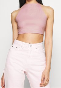 Top corto rosa con tirantes, hecho de un material brillante, combinado con unos vaqueros de tiro alto rosa claro que cuentan con bolsillos delanteros y detalles en hardware plateado.