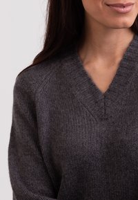 Maglione grigio in lana con scollo a V, caratterizzato da una trama a coste e una vestibilità leggermente ampia, che enfatizza un aspetto accogliente e confortevole.