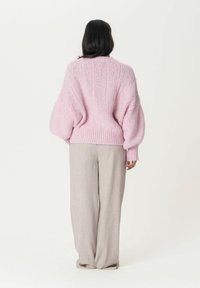 Pull en tricot rose avec une texture chunky et des manches oversized, associé à un pantalon large gris clair, vu de derrière.