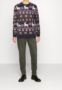 Marinblå stickad tröja med vintertema, prydd med vita renar, snöflingor och röda samt gröna accenter. Matchad med grå byxor och svarta stövlar.