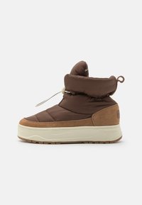 Bota de invierno acolchada marrón con ribete de ante beige, suela gruesa blanca, cordón ajustable con toggle y tirador en la parte trasera sobre un fondo blanco.