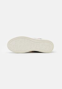 Semelle de sneaker en caoutchouc blanc texturé avec le mot "GUESS" embossé sur toute la surface. Forme arrondie avec une légère arche et des bords renforcés.