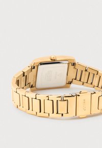 Goudkleurig rechthoekig polshorloge met metalen schakelarmband. Heeft een gladde textuur, een opvallende lunette en een gepolijste afwerking.