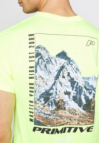 Neon žluté tričko s krátkým rukávem s grafiku hory na zadní straně, textem "OVLÁDNĚTE SVOU VYSOKOU EST 2008" a logem značky "P."