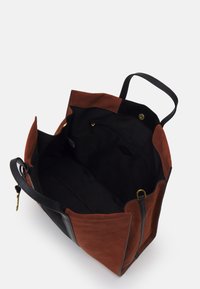Sac fourre-tout avec des côtés en daim marron et des accents en cuir noir. L'intérieur est doublé de tissu noir avec une poche zippée et des finitions dorées.