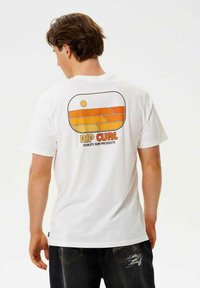 Hvid bomulds t-shirt med et retro-stil orange og gult grafisk print på ryggen med teksten "RIP CURL" og "QUALITY SURF PRODUCTS."