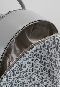 Grå texturerad ryggsäck med dragkedjestängning, med en inre foder i en slät, ljus färg och ett mönstrat ytterfoder i svart och vitt.