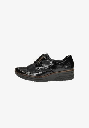 Zapato de charol negro con una tira de Velcro, punta redondeada y superficie texturizada. Cuenta con una suela acolchada y sutiles acentos marrones.