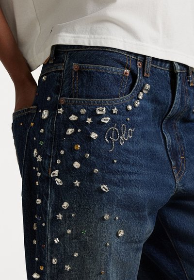 Tmavomodré džínsy z denimu s rozptýlenými rhinestonovými ozdobami rôznych tvarov, veľkostí a farieb. "Polo" je vyšívané striebornou niťou.