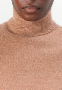 Sweter z golfem wykonany z miękkiej, jasnobrązowej tkaniny, z delikatnym prążkowaniem przy kołnierzu. Gładka tekstura z minimalnymi detalami.