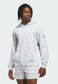 Svetlošedá mikina s kapucňou a abstraktným vzorom, klokanie vrecko, logo na hrudi a rebrované manžety. V spolupráci s ladícími šortkami.