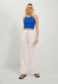 Niebieski krótki top na ramiączkach zestawiony z białymi spodniami typu wide-leg. Modelka nosi czarne klapki. Miękkie tekstury, minimalistyczny design i luźny krój.