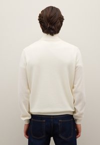 Gestrickter cremefarbener Pullover mit hohem Kragen, gerippten Bündchen und Saum. Die Rückseite weist eine glatte Textur und ein neutrales Design auf.