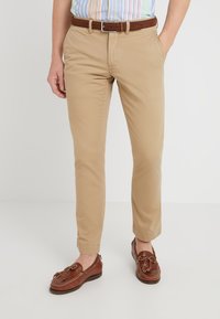 Khaki chino's met een slim fit, voorzien van een zachte textuur, omslag aan de pijpen en een bruine leren riem. Gecombineerd met bruine loafers.