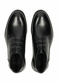 Zapatos de piel negra con acabado pulido, que presentan cuatro ojetes, puntera redondeada y un diseño minimalista. Forro interior suave visible.