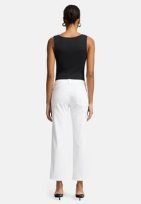 Top senza maniche nero abbinato a jeans bianchi a vita alta e gamba dritta. Tessuto morbido con una silhouette aderente. Tacchi neri completano il look.