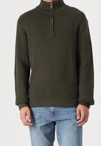 Pull-over en maille vert olive avec une demi-fermeture éclair, motif texturé, poignets et ourlet côtelés. Coupe décontractée, manches longues, style casual.