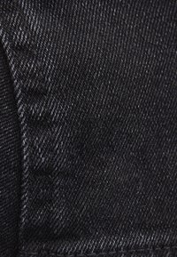 Närbild på svart denimtyg som visar en slät textur med subtila horisontella och vertikala vävmönster. Synliga sömmar längs kanterna.