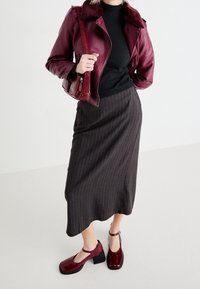 Vinskark leather jacket med konstgjord pälskrage, svart ribbat linne, grå randig kjol och röda klackskor med ankelremmar.