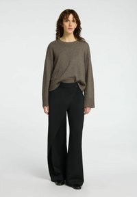 Maglione marrone a maglia con una vestibilità ampia, abbinato a pantaloni neri a vita alta con un taglio asimmetrico e un dettaglio con bottone.
