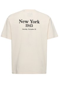 Camiseta de manga corta color crema con texto negro que dice "Nueva York 1945" y "Sábado, 22 de diciembre" en la parte trasera. Corte regular, material de algodón.