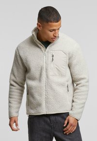 Fleecejakke i off-white med en struktureret overflade, høj krave, en frontlomme med lynlås og sidelommer med lynlås; afslappet pasform.